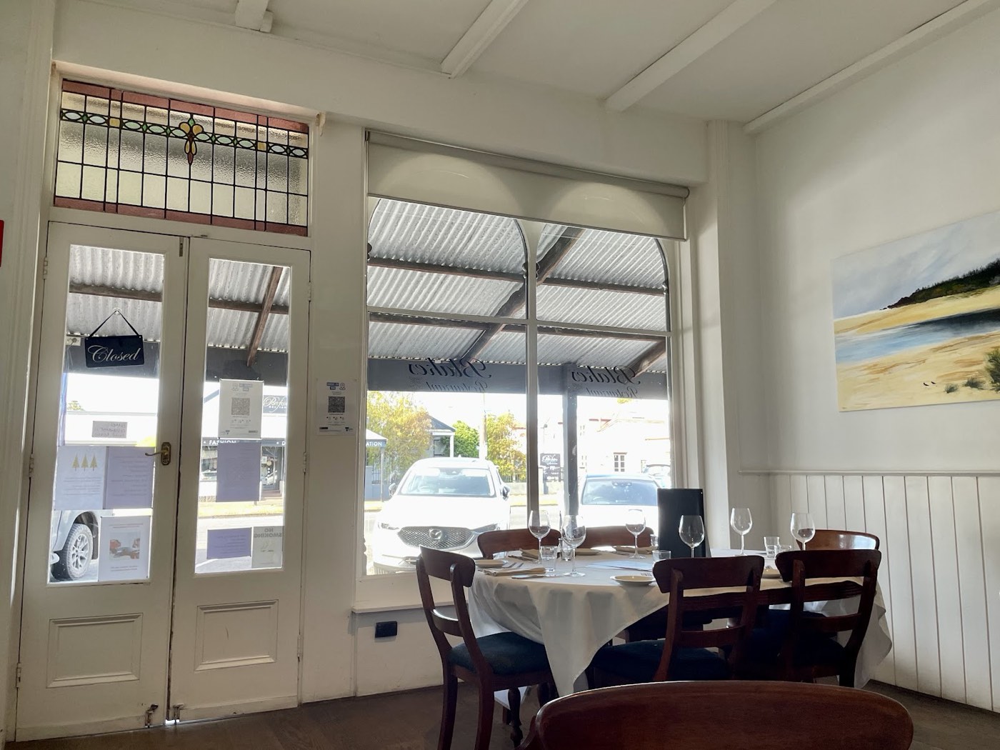 The dining room with white walls, round tables set with glasses, and French doors with stained-glass panels
